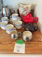 Group shot showing bone china cups and saucers, two teapots, metal creamer and sugar bowl, stainless insulated pitcher