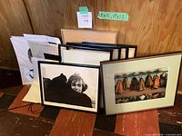 Stack of six framed prints/photos leaning against wall