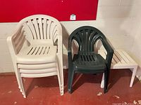Stack of five off-white chairs, one dark green chair, white side table