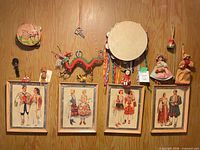 Overview of wall-mounted lot with tambourines, marionette, dolls and four framed prints