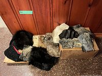 Two boxes containing assorted fur pelts and shearling pieces against wood paneling