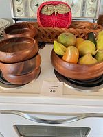 Stack of four small wooden bowls, large wooden bowl filled with faux fruit, wicker tray, red apple-shaped wicker basket