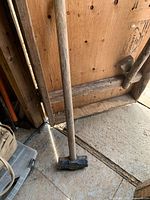 Full view of sledgehammer leaning against plywood wall