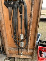 Full view of long black heavy-gauge extension cord hung vertically, showing overall length and both inline metal outlet boxes