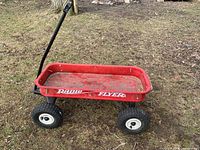 Full view of red Radio Flyer wagon with handle and pneumatic tires on grass