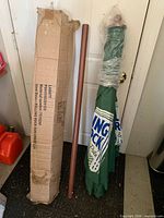 Umbrella pole, boxed canopy, and wrapped canopy leaning against door