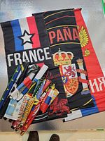Group of unrolled large banners for France, Spain, Russia with pile of rolled banners and poles