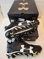 Two shoe boxes stacked with pair of black/white/yellow Under Armour cleats displayed
