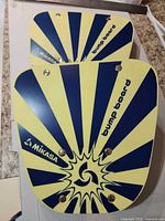 Front view of two Mikasa bump boards showing yellow and blue graphics and screw hardware
