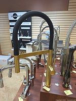 Front view of Grohe brushed gold faucet with black hose on display board