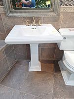Overall view of Kohler white pedestal sink with faucet mounted in tiled bathroom corner