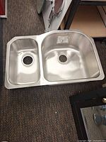 Top view of brushed stainless double-bowl sink showing both bowls, rim, and factory sticker