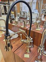 Full view of polished brass faucet with black pull-down hose mounted on display board