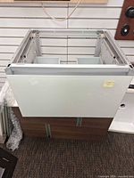 Front view of vanity cabinet showing white gloss glass drawer front, aluminum frame and brown wood sides