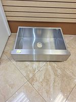 Top and front view of brushed stainless apron-front single-bowl sink showing center drain