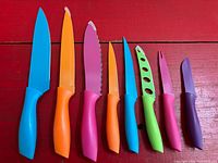 Seven brightly colored kitchen knives laid out showing full blades and handles