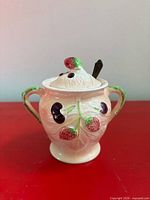 Front view of pink ceramic sugar bowl with berry motifs and green handles