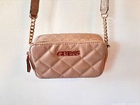 Front view of mauve quilted GUESS crossbody bag hanging, shows size and overall style