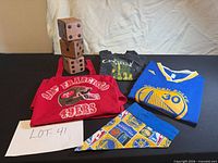 Group shot of all items: jersey, two T-shirts, bandana, five wooden dice/blocks