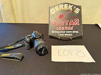 Lot overview showing Nikon DSLR with lens, strap, sign, paper lot number