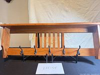 Front view of wood shelf showing slatted back and five metal hooks