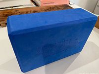 Front angled view of blue foam yoga block showing color, shape and logo