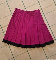 Full view of pink pleated wool skirt showing black hem
