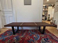 Full view of slatted wood bench with black legs on rug