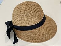 Front angled view of tan synthetic wicker sun hat with black ribbon bow