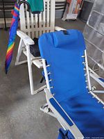 Blue reclining lounge chair, partial view of white lawn chair and rainbow umbrella