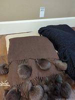 Brown throw with faux fur pom-pom fringe atop black knit throw