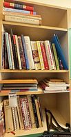 Entire bookshelf showing three shelves of assorted cookbooks, spiral notebooks and folders