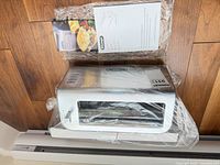 Top view of toaster sealed in plastic with manual and basket on wood floor
