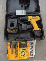 Open DeWalt case showing drill-driver with battery, spare battery, charger, drill bit set and manuals