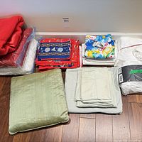 Grouped view of folded red set, blue printed quilt, floral duvet set, packaged mattress pad, green pillow and grey sheets