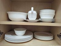 Stacked bowls, plates, covered sugar bowl, large serving bowl on cabinet shelves