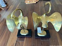 Front view of both brass swan sculptures showing wing shapes and black bases