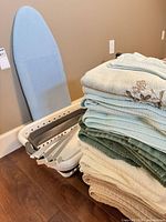 Ironing board, stack of towels, collapsible basket and rack