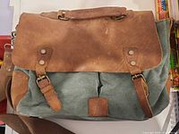Front view of green canvas bag with brown leather flap, buckle straps and shoulder strap