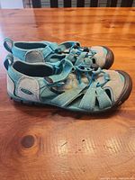 Side view of both sandals showing teal webbing, gray suede, black toe caps