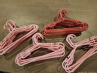 Four bundled stacks of pink and magenta child-size plastic hangers on wood surface