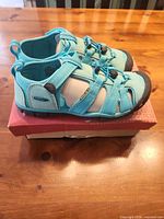 Side view of pair of turquoise KEEN sandals on original box