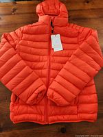 Front view of orange puffer jacket with hood and tags
