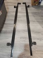 two black steel twin bed rails laid out side by side on floor