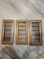 Three bronze-tone metal louvered vent registers laid side by side showing front view and surface wear