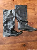 Pair of black knee-high slouch flat boots laid flat showing outer sides and soles