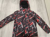 Front view of youth ski jacket with hood, showing geometric black red gray pattern