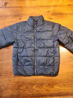 Front view of navy puffer jacket showing zipper, quilting, stand collar