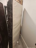 Twin box spring standing upright showing beige side and dark patterned border
