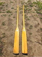 Full view of both wooden oars laid side by side on ground